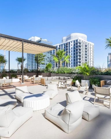 Rooftop terrace with lounge seating, pergola shade, palm trees, and city skyline views