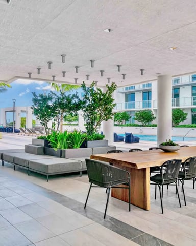 Covered outdoor terrace with dining table, lounge seating, fire pit, and pool view overlooking waterfront buildings