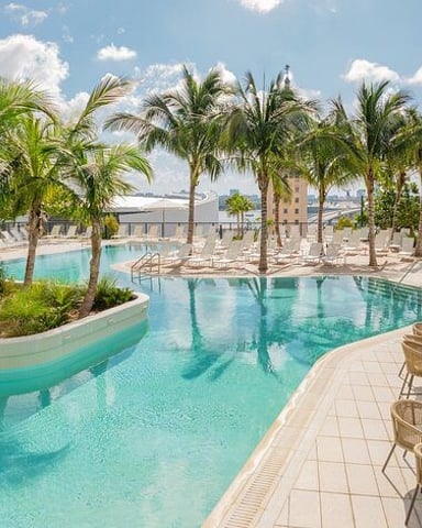 Resort pool with turquoise water, palm trees, lounge chairs, and mountain views under blue sky