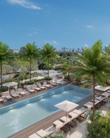 Resort pool with loungers and palm trees, city skyline visible in distance under blue sky
