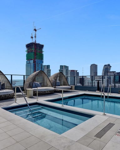 Rooftop pool deck with woven lounge pods, two pools, and downtown city skyline view