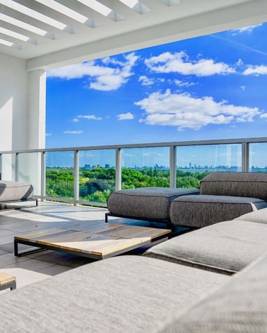 Modern rooftop lounge with gray seating, city skyline view, and blue sky with clouds