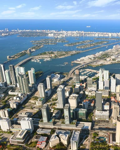 Aerial view of coastal city with high-rise buildings, blue water, islands, and cruise ship in harbor