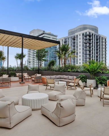 Rooftop terrace with lounge seating, retractable awning, palm trees, and city skyline views