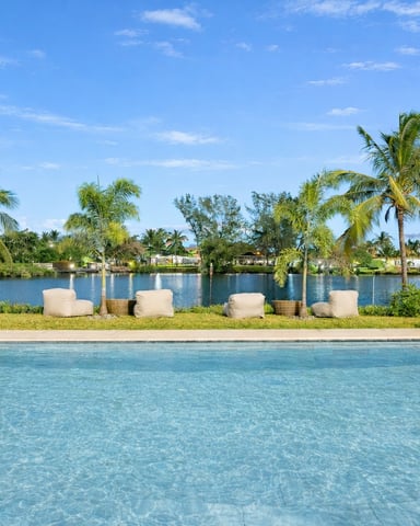 Swimming pool with waterfront view, palm trees, lounge chairs, and residential homes across the canal