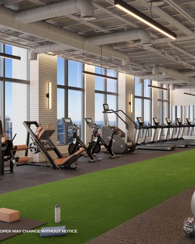 Modern gym with cardio equipment, exercise bikes, treadmills, green turf area, and city skyline views through floor-to-ceiling windows.